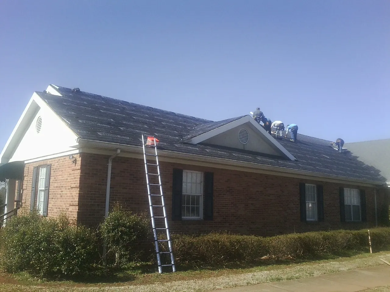 Crew tearing shingles off a brick ranch roof with a ladder set — Emergency Roof Repair work by our crew in Loretto