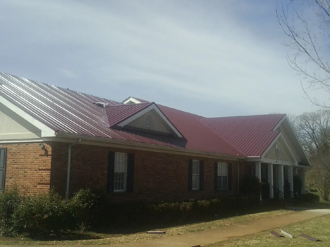 Red metal roof with gabled entries on a long brick building, from a Hail Damage Roof Repair job in Loretto