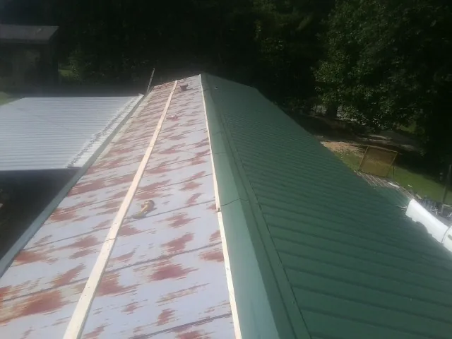 Old rusted panels beside newly installed green metal roofing — Wind Damage Roof Repair by Roofing Brothers in Loretto