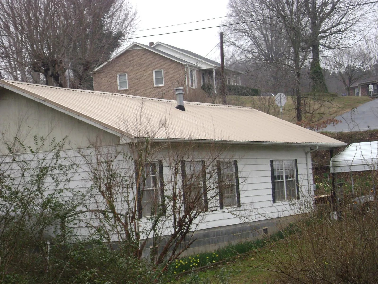 Tan metal roof on a white sided house set into a hillside — Commercial Roofing by Roofing Brothers in Loretto